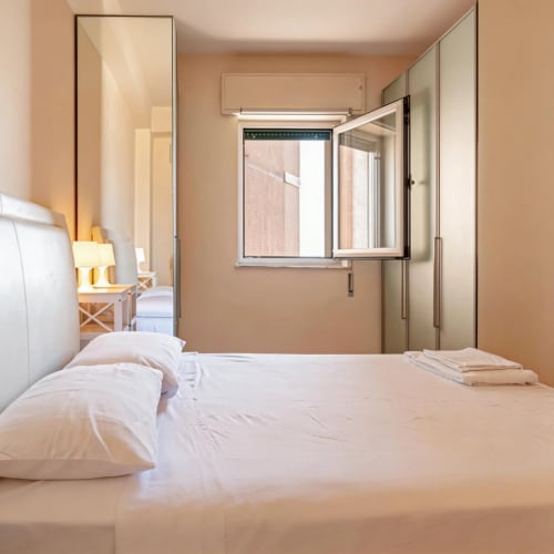 Bright modern bedroom at Roby's Panoramic House in Livorno with white bedding, large mirror, and city view window