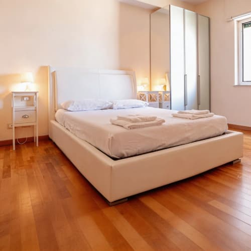 Modern bedroom with cream upholstered bed, mirrored wardrobe, wooden flooring, and warm lighting at Roby's Panoramic House in
