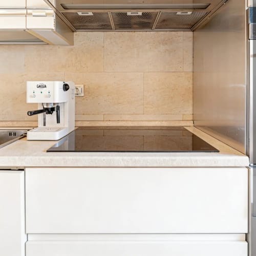 Modern kitchen with white Gaggia espresso machine, travertine backsplash, and light wood countertops at Roby's Panoramic