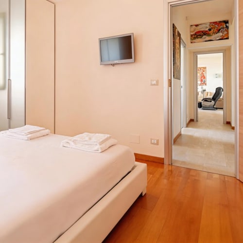 Spacious bedroom with white bedding, flat-screen TV, wooden floors, and open doorway in Roby's Panoramic House apartment,