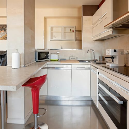 Modern kitchen with white cabinets, red bar stool, and stainless steel appliances at Roby's Panoramic House in Livorno
