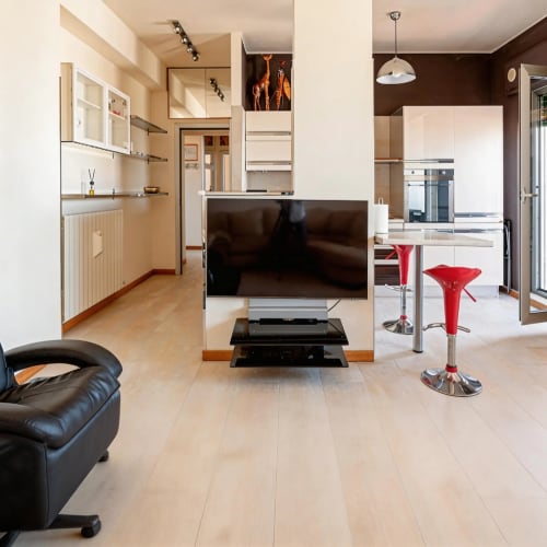 Modern open-plan apartment in Livorno with kitchen, living area, flat-screen TV, black leather chair, and red bar stools