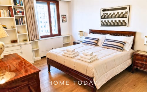 Spacious bedroom in Padova apartment with wooden bed, striped pillows, cream bedding, and city views from windows