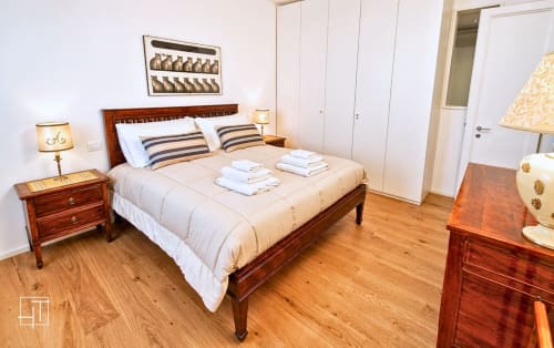 Elegant bedroom in Padova apartment with wooden bed, striped pillows, white bedding, wooden nightstands with lamps, and