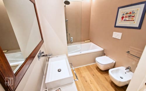 Modern bathroom in Padova apartment with wooden flooring, white fixtures, bathtub, bidet, toilet, and glass shower enclosure