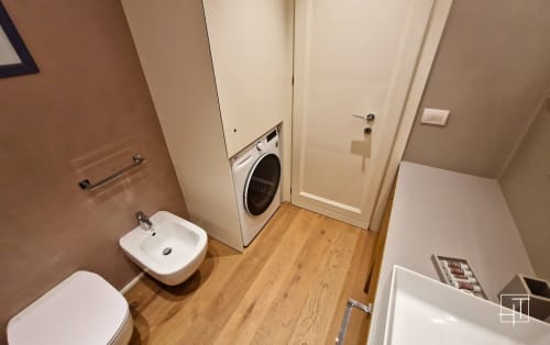 Compact apartment laundry room with washing machine, white sink, wooden flooring, and cream-colored doors in Padova property