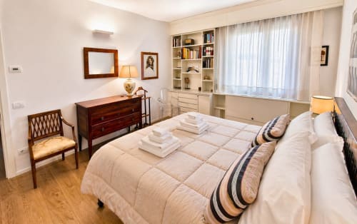 Bright bedroom in Padova apartment with queen bed, wooden dresser, bookshelves, and city views through large windows