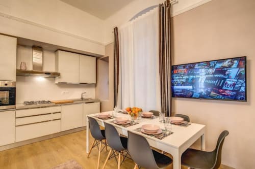 Modern kitchen-dining area in Rome apartment with white cabinetry, dining table set for four, and wall-mounted TV