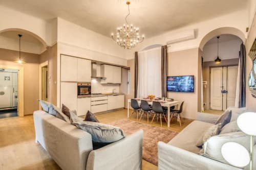 Modern apartment living room with dining area, kitchen, beige sofas, and chandelier in Roma - Cinque Terre New Liberty