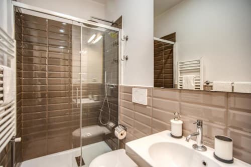 Modern bathroom in Rome apartment with brown tile shower, dual white sinks, and contemporary fixtures