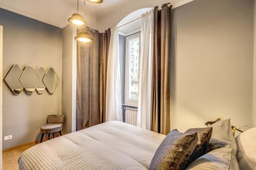 Modern bedroom in Cinque Terre apartment with striped bed, gold pendant lights, arched window, and decorative mirrors