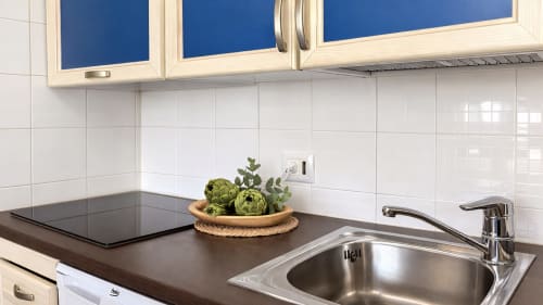 Cocina moderna en apartamento Holidays Costa Brava con encimera oscura, fregadero de acero inoxidable y azulejos blancos