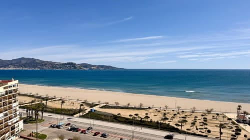 Playa de Empuriabrava con mar turquesa, costa arenosa y pueblo costero en ladera, vista desde balcón de Holidays Costa Brava