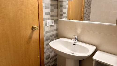 Baño moderno en Holidays Costa Brava con lavamanos pedestal, azulejos grises y puerta de madera en Empuriabrava