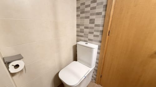 Baño moderno en Holidays Costa Brava, Empuriabrava con inodoro blanco, detalles de mosaico y azulejos en tonos crema