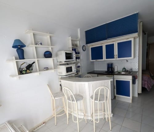 Cocina y comedor moderno en apartamento de Holidays Costa Brava con muebles blancos, detalles azules, barra y vistas al mar