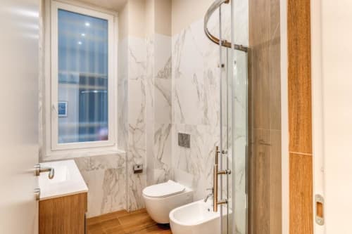 Bagno moderno con pareti in marmo, box doccia in vetro e finiture in legno nell'appartamento di Roma