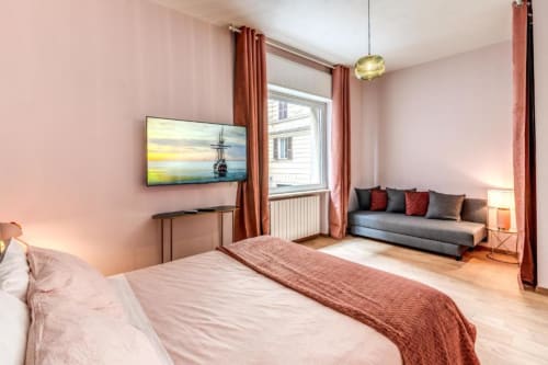 Spaziosa camera da letto nell'appartamento Croce di Malta Royale a Roma, con pareti rosa, letto, divano grigio, TV e vista sul giardino
