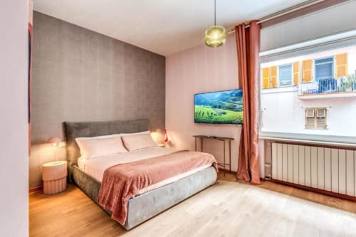 Camera da letto moderna in appartamento romano con letto queen, pareti rosa, TV, vista sul giardino e pavimenti in legno