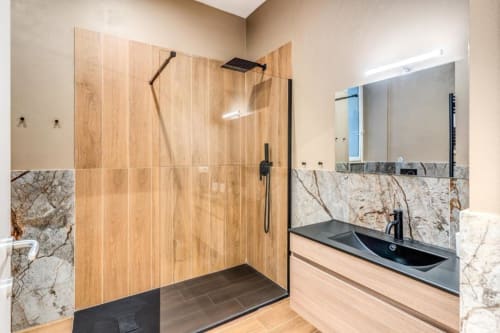 Bagno moderno con doccia in legno e piastrelle, dettagli in marmo, rubinetteria nera e lavabo ad onda nell'appartamento di Roma