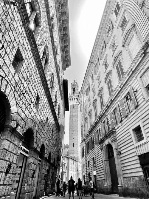 Historic Italian street with tall buildings and bell tower visible in distance, Pozzo della Chiana