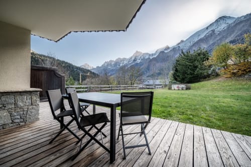 Wooden deck with outdoor dining table and chairs overlooking alpine mountains at Le Chalet Mont-Blanc in Chamonix
