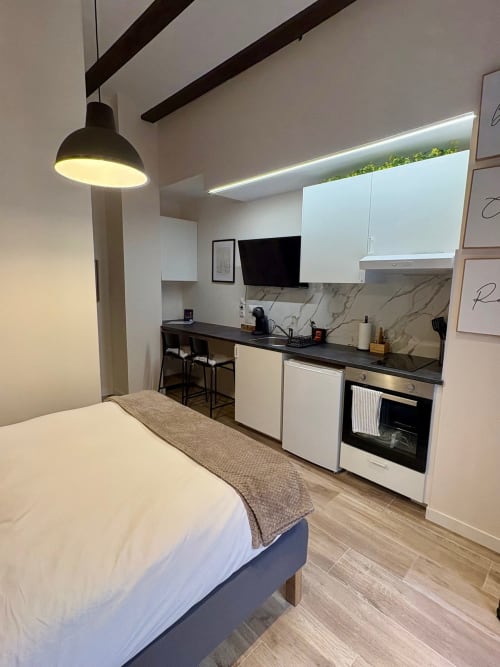 Moderno estudio con dormitorio, cocina integrada, encimera negra, armarios blancos y cama en Be Gonfre Flats Valencia