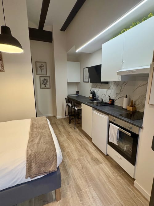 Moderno apartamento estudio en Be Gonfre Flats Valencia con cama, cocineta, encimera negra, armarios blancos y detalles de madera
