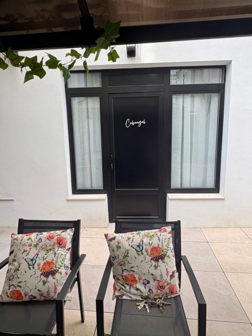 Entrada de puerta negra a la habitación Cabanyal en Be Gonfre Flats con asientos tapizados de flores y hiedra trepadora en Valencia