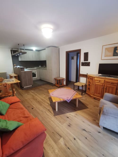 Ampio soggiorno con pavimenti in legno, cucina, TV e arredi colorati ad Auronzo di Cadore