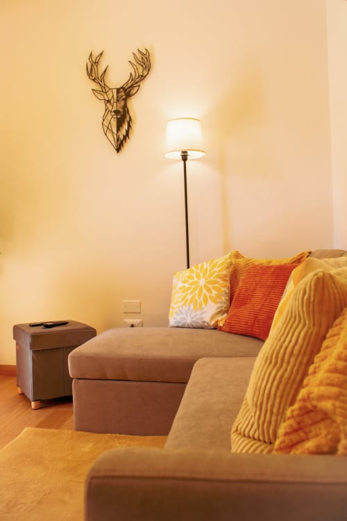 Gemütliches alpines Wohnzimmer in Pieve di Cadore mit beigem Sofa, gelben Kissen, Stehlampe und geometrischer Hirsch-Wandkunst