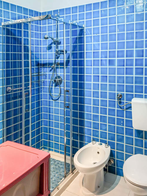 Modern blue tiled bathroom with walk-in shower, bidet, and toilet at Vesta Home Rent in Padova