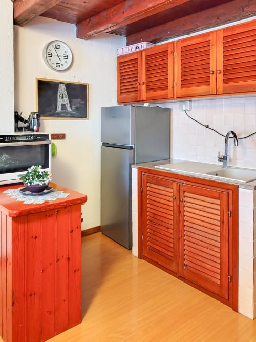 Bright kitchen with red wooden cabinets, stainless steel refrigerator, and wood beams at Vesta Home Rent, Padova