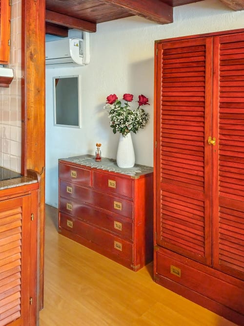 Vesta Home Rent Dolce Sardinia apartment bedroom with red wooden furniture, white vase with roses, and wooden beams
