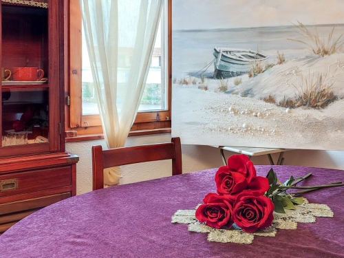 Elegant Dolce Sardinia apartment at Vesta Home Rent Padova with red roses on purple tablecloth, sea view painting, and