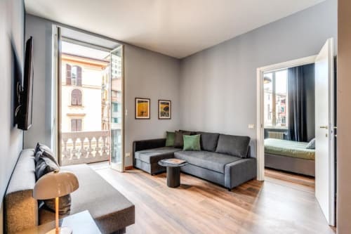 Modern apartment living room in Rome with city balcony view, gray sofa, wooden floors, and contemporary furnishings