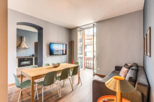 Modern Roma apartment living area with wooden dining table, gray sofa, wall-mounted TV, and city balcony view