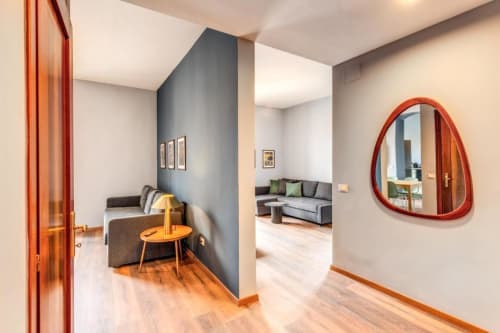 Modern Roma apartment hallway with red-framed mirror, gray accent wall, wooden floors, and open-plan living area in Cinque