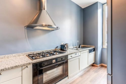 Modern kitchen in Roma apartment with stainless steel range hood, gas cooktop, granite counters, and blue accent walls