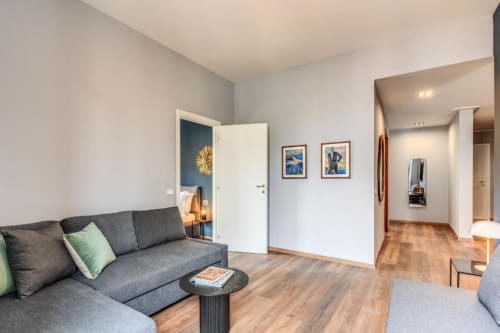 Modern apartment living room with gray sofa, wooden floors, and blue accent door in Roma's Cinque Terre Dream apartment