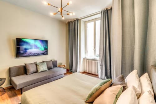 Spacious bedroom in Roma apartment with bed, gray sofa, flat-screen TV, city view, and modern furnishings