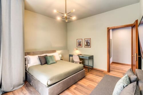 Modern bedroom in Rome apartment with queen bed, wooden floors, desk, and city view through open doorway
