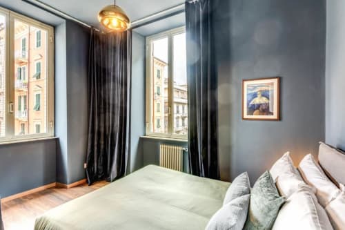 Modern bedroom in Rome apartment with city views, brass pendant light, dark curtains, and contemporary furnishings