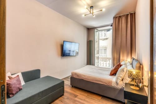 Modern bedroom in Roma apartment with city view, bed, sofa, wall-mounted TV, and balcony access