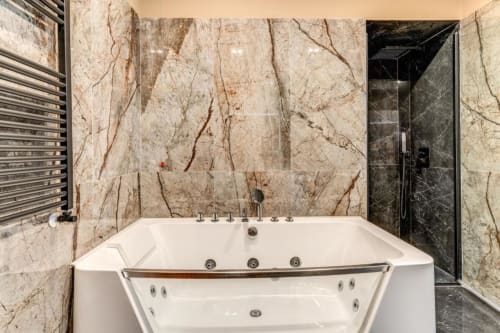 Luxury bathroom with marble walls, white jacuzzi tub, and dark shower enclosure in Roma apartment