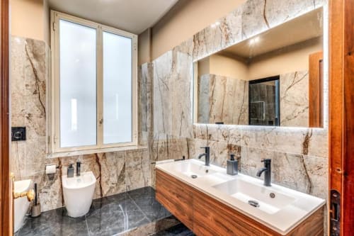Modern bathroom in Cinque Terre Dream apartment with marble walls, double sink, illuminated mirror, and city views from