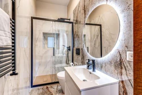Modern bathroom in Cinque Terre Dream apartment with marble tiles, illuminated mirror, white sink, and glass shower enclosure