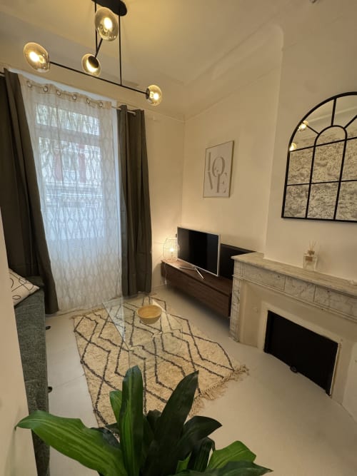 Cosy cottage living room with fireplace, TV, modern lighting, patterned rug, and plants in Bouc Bel Air