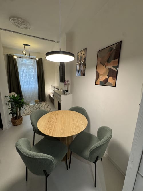 Modern dining area with round wooden table, green upholstered chairs, pendant light, and city view at Cosy Cottage by Alice