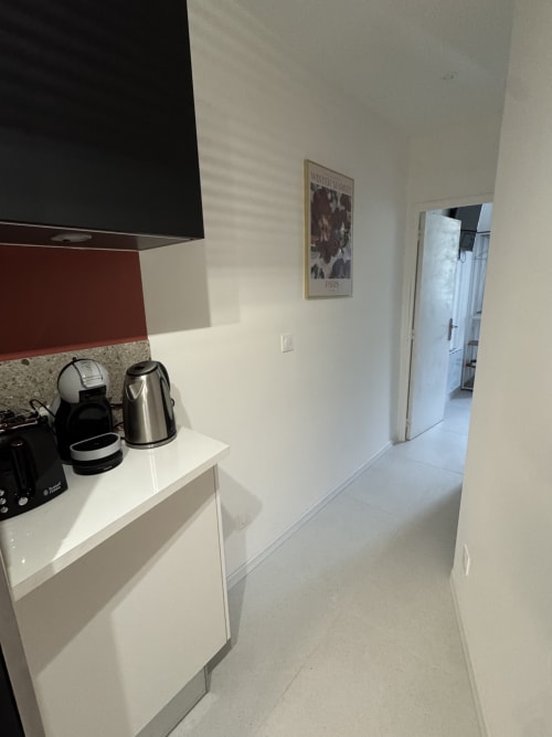 Modern kitchenette in Cosy cottage by Alice with white cabinets, red backsplash, coffee maker, kettle, and open doorway to